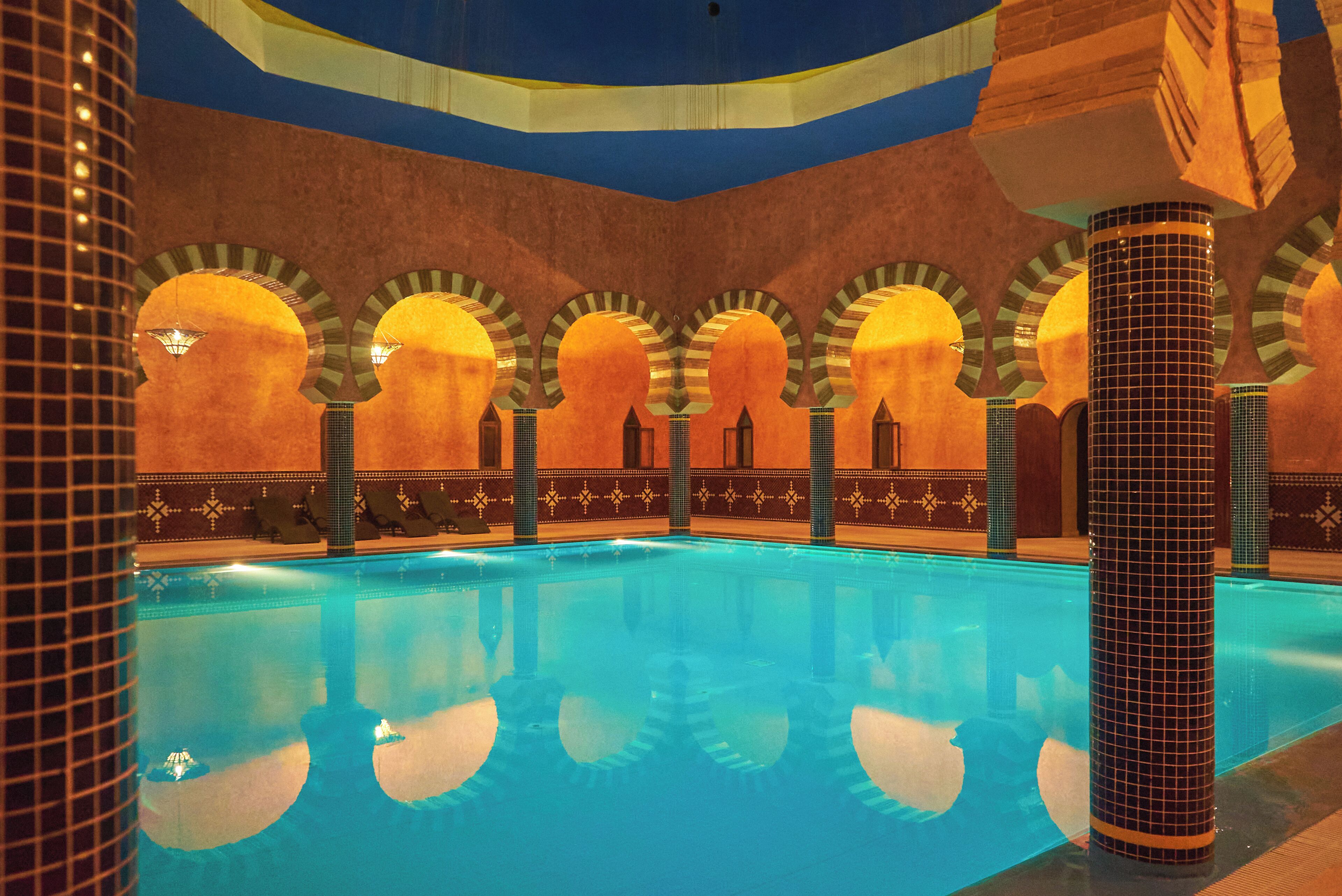 A swimming pool with a tiled floor and walls, surrounded by arches and columns.