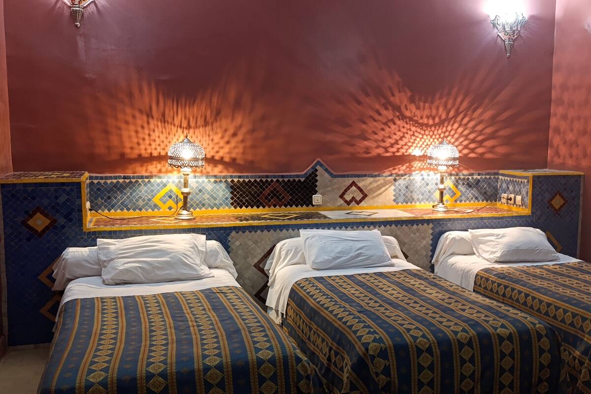 Une chambre avec deux lits, un mur recouvert de carreaux et un lustre.