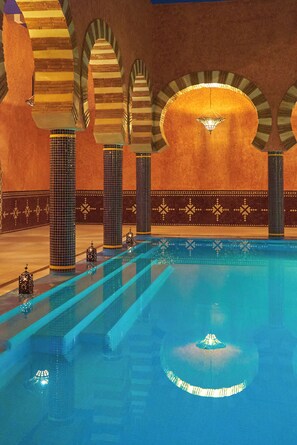Une piscine aux murs et aux colonnes recouverts de carreaux, et une fontaine centrale.
