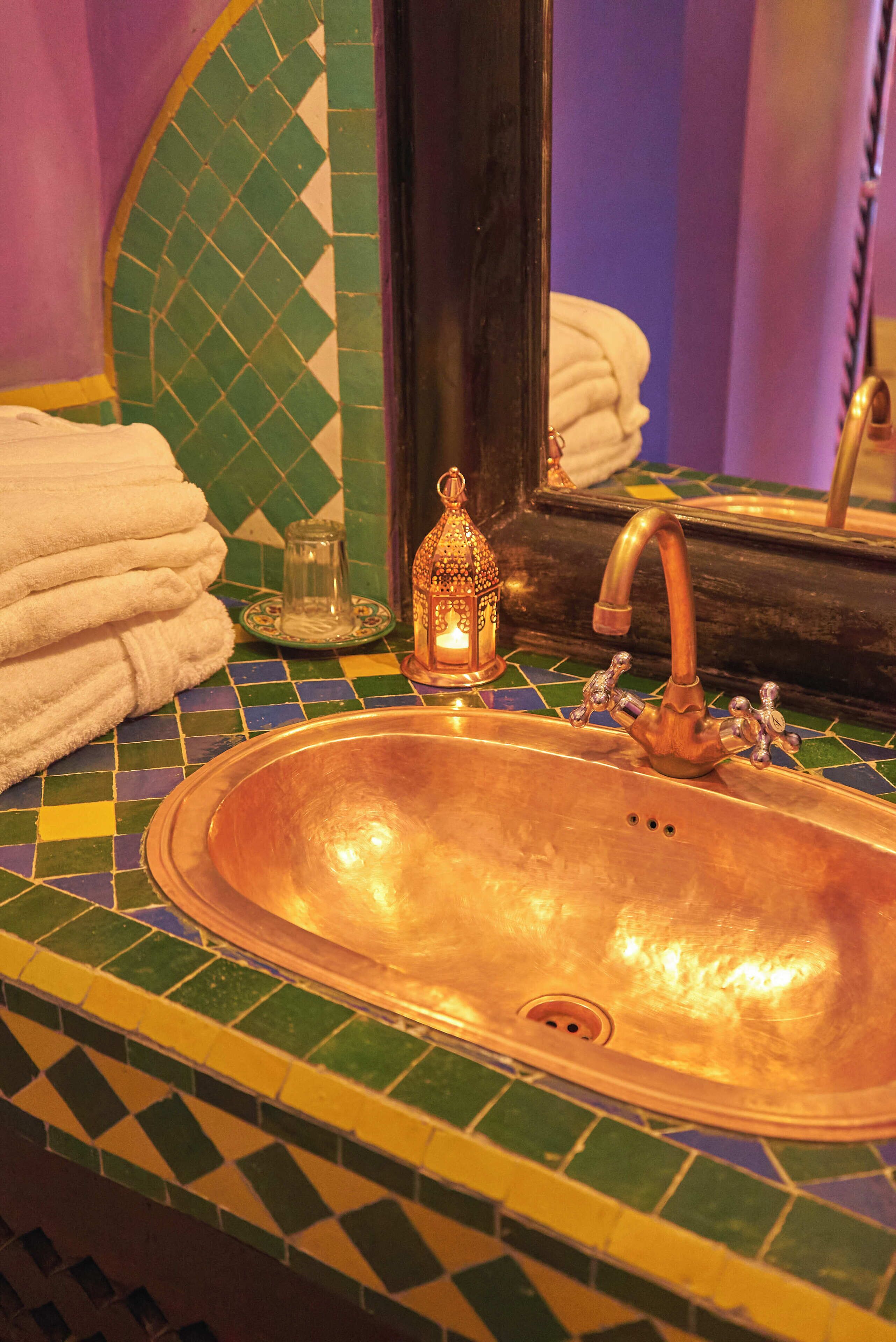 Un baño con lavamanos de cobre, un espejo y un respaldo de azulejos.