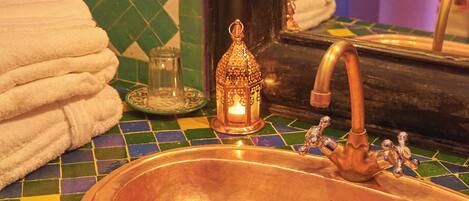 Un baño con lavamanos de cobre, un espejo y un respaldo de azulejos.