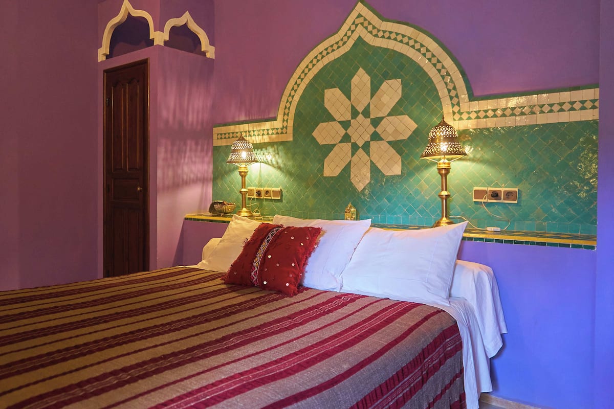 Un lit avec une couvre-lit à rayures, deux lampes de chevet et un mur décoratif orné d’un motif géométrique.