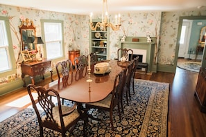 A dining room with a wooden table, chairs, a chandelier, and a floral wallpaper.