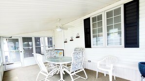 Un patio coperto con un tavolo rotondo e sedie, una ventola a soffitto e vista attraverso le porte in vetro.