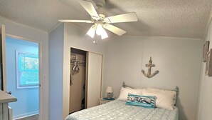 Camera da letto con un letto, una ventola a soffitto, un comodino, una lampada e un elemento decorativo fissato alla parete.
