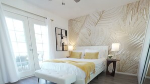 Een slaapkamer met een bed, een plafondventilator, een nachtkastje en een muur met een bladmotief.