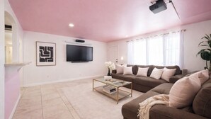 Een woonkamer met een bruine bank, een salontafel, een flatscreen televisie en een plafondprojector.
