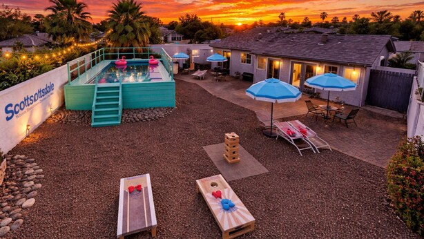 Een achtertuin met een zwembad, lounge stoelen, parasols en een bord met Scottsdale.
