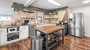 Eine moderne Küche mit weißen Schränken, Edelstahlgeräten, einer Holzinsel und einem einzigartigen Wanddesign in Grün- und Beigetönen.
