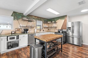 A modern kitchen with white cabinets, stainless steel appliances, a wooden island, and a unique green and beige wall design. - Blue Tide House & Coral Cottage Family Compound on Canal & 1/2 mile to the beach (St. Augustine)