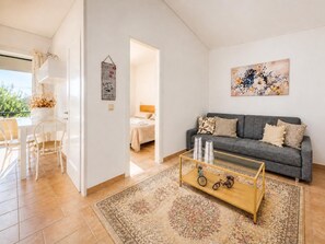 A modern living room with a grey sofa, a coffee table with decorative items, a patterned rug, and a painting on the wall. - Golden Tiara Apartment (Mparmpati)