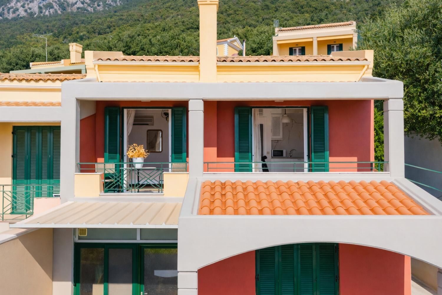 A two-story building with a balcony, green shutters, and a tiled roof.