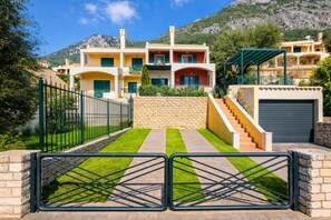 A multi-story residential building with a stone wall, a gated entrance, and a staircase leading to the entrance. - Golden Tiara Apartment (Mparmpati)