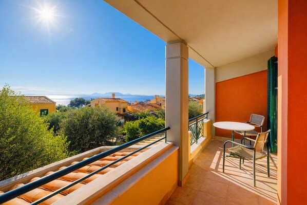 Ein Balkon mit Meerblick und Gebäuden, ein Tisch mit Stühlen und einem Geländer.