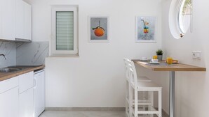 A modern kitchen with white cabinets, a marble countertop, a dining area with a wooden table and chairs, and two framed artworks on the wall. - Sunny Palace Studio 1 (Dubrovnik)