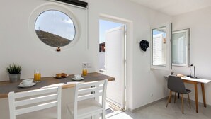 A room with a dining table, chairs, a round window, a door, and a desk with a chair. - Sunny Palace Studio 1 (Dubrovnik)