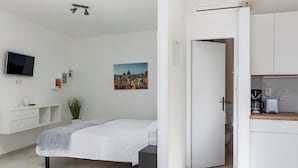 A modern bedroom with a bed, bedside tables, a TV, and a cityscape painting. - Sunny Palace Studio 1 (Dubrovnik)