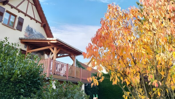 Un chalet traditionnel doté d’un balcon, entouré du feuillage automnal.