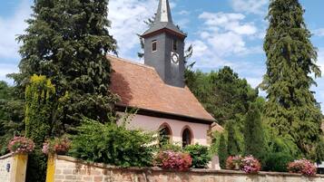 Une église dotée d’un clocher, entourée de murs de pierre et de grands arbres.