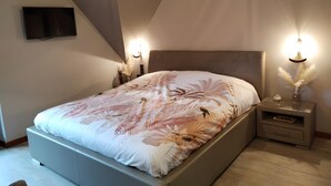 Une chambre à coucher comprenant un lit, un téléviseur à écran plat, une table de chevet et une lampe fixée au mur.