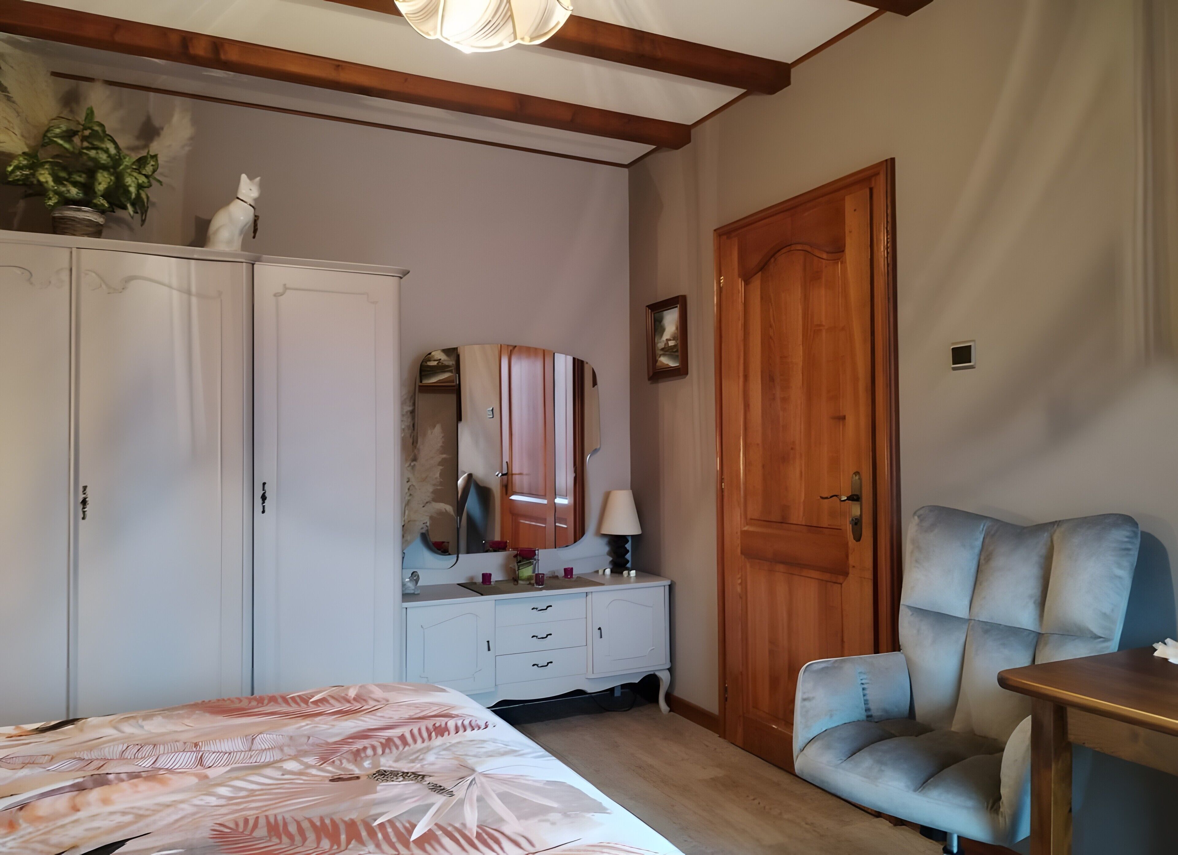 Ein Schlafzimmer mit einem Bett, einem Schminktisch, einem Spiegel, einer Holztür und einem blauen Sessel.