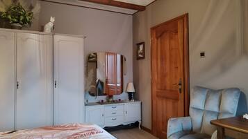 Ein Schlafzimmer mit einem Bett, einem Schminktisch, einem Spiegel, einer Holztür und einem blauen Sessel.