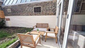 A patio with a table and chairs, a small potted plant, and a brick wall with a window. - Delightful 1-Bedroom w/ Garden in Queen’s Park near Notting Hill & Little Venice (London)