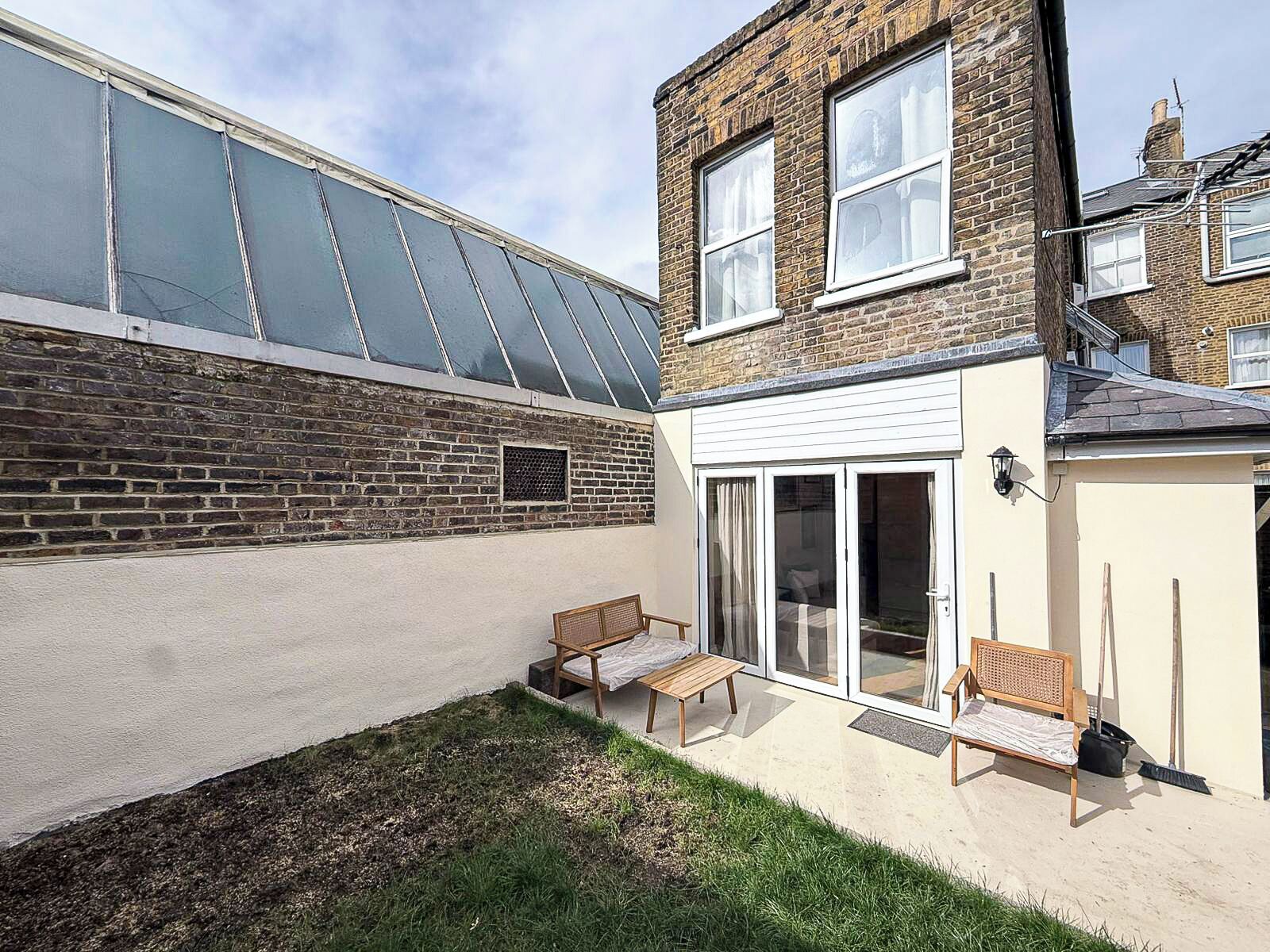 A two-story brick house with a conservatory, a patio with a bench, and a sliding glass door leading to a room.