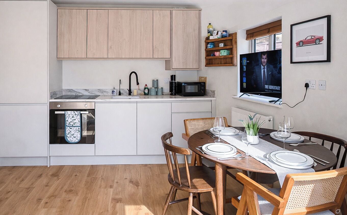 A modern kitchen with white cabinets, a built-in microwave, and a dining area with a wooden table set for four.