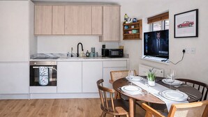 A modern kitchen with white cabinets, a built-in microwave, and a dining area with a wooden table set for four. - Delightful 1-Bedroom w/ Garden in Queen’s Park near Notting Hill & Little Venice (London)