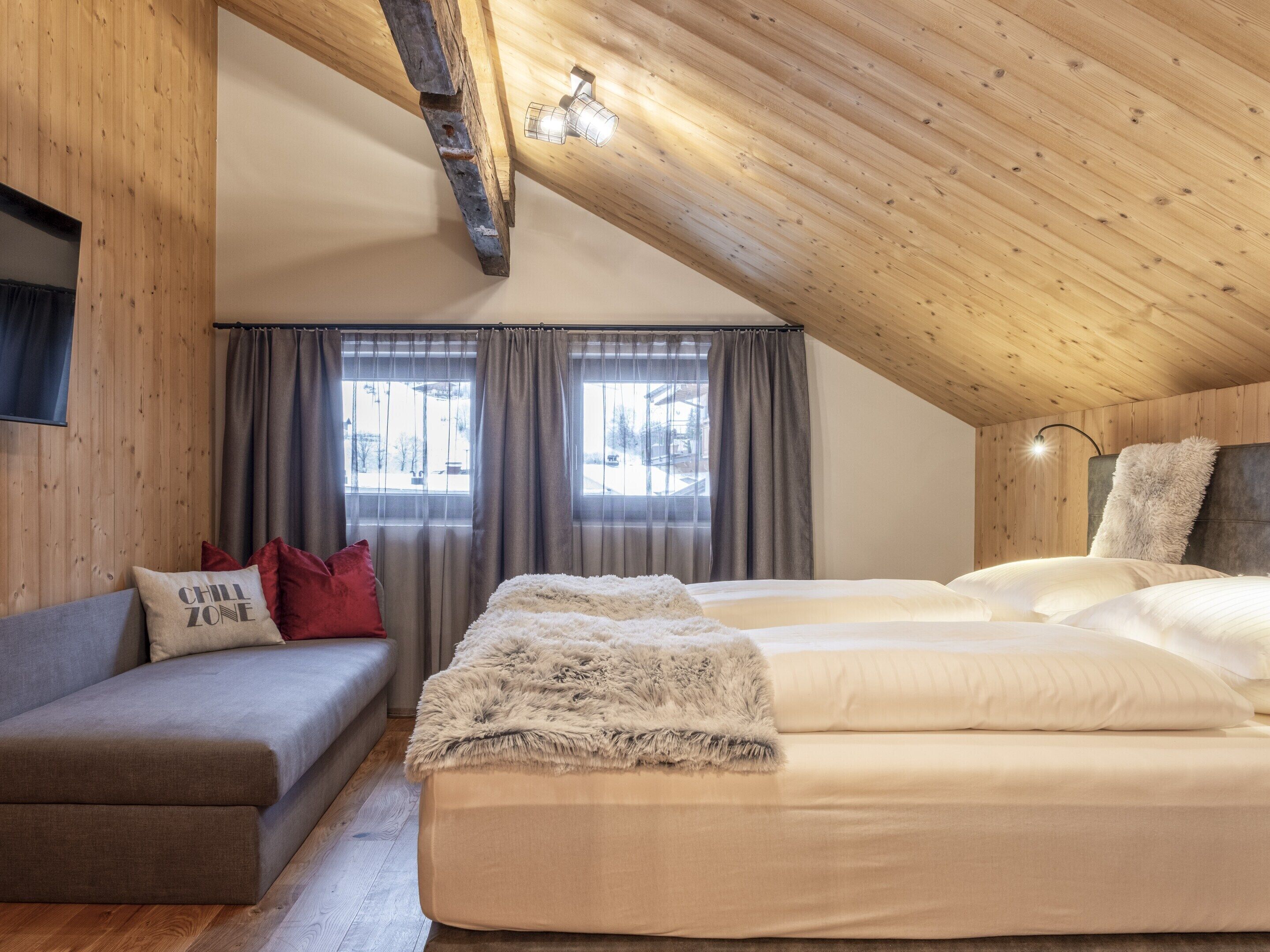 A cozy room with a sloped ceiling, a sofa, a bed with fluffy bedding, and a window with curtains.