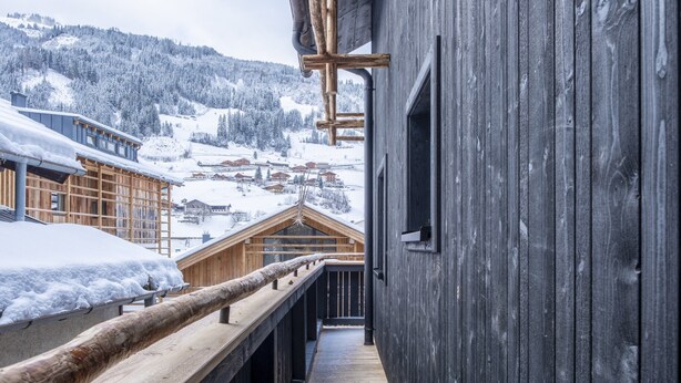 Ein Holzbalkon mit Blick auf schneebedeckte Gebäude und einen bewaldeten Berg im Hintergrund.
