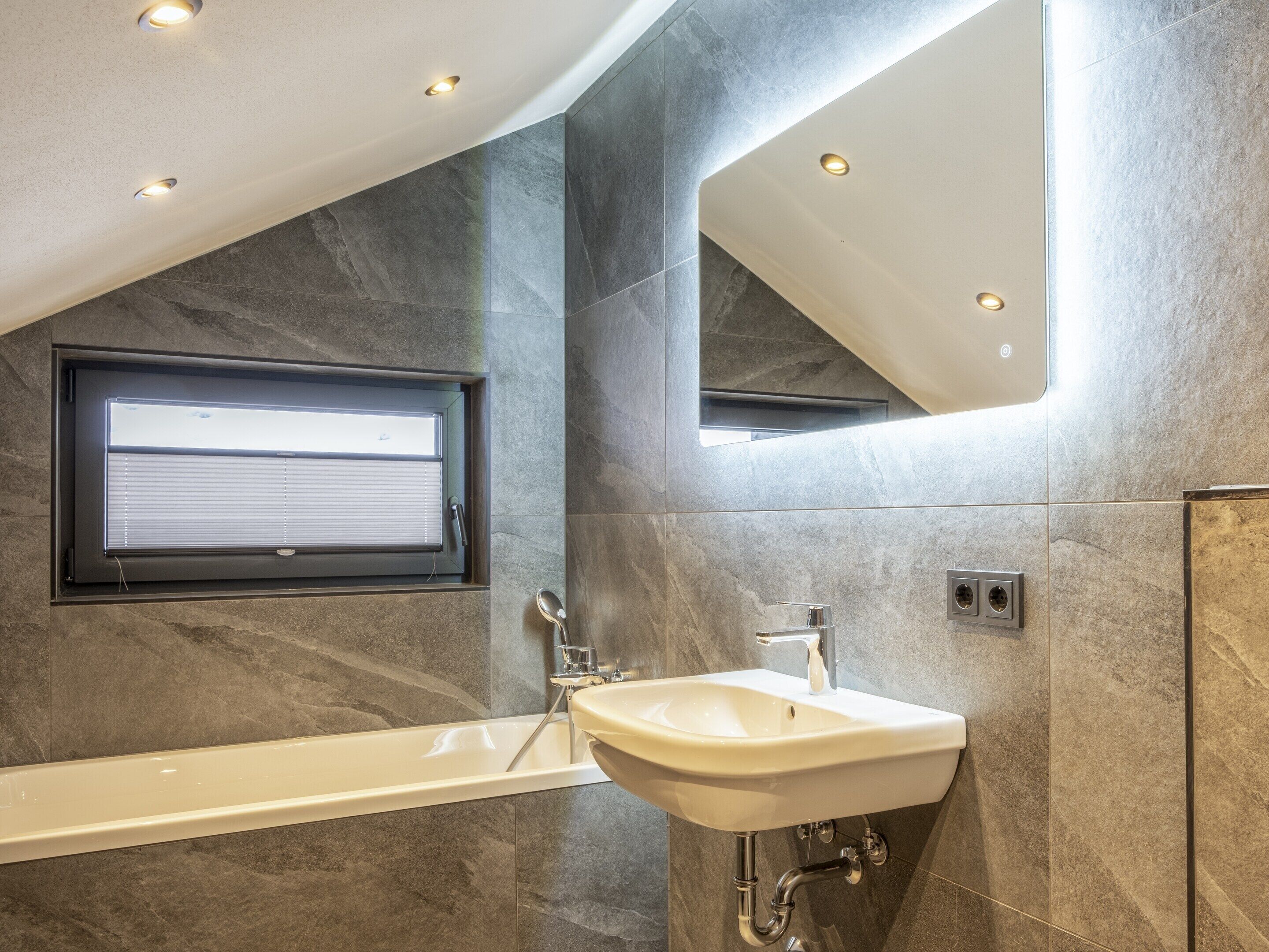 Une salle de bain moderne avec une baignoire, un lavabo et une fenêtre équipée de stores.