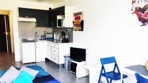 Pieni hotellihuone, jossa on minikeittiö, sinisillä tekstiileillä varustettu sänky, pieni televisio ja tuoli.