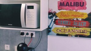 A kitchen with a microwave, a coffee machine, and a wall with colorful signs indicating different beach locations. - White and blue studio 1min from the promenade and the beach !😎 (Nice)