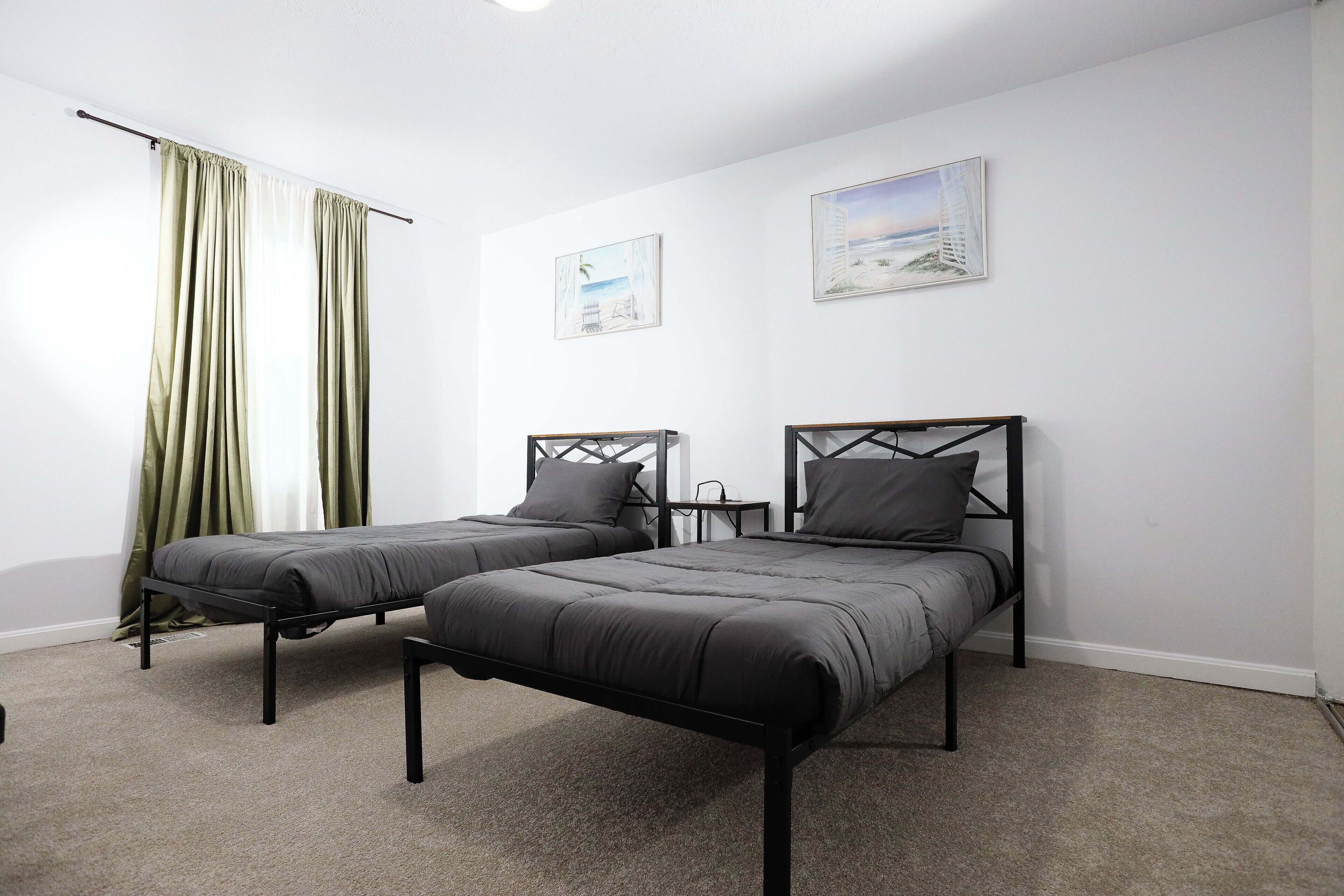 A room with two single beds, a small table, and two paintings on the wall.