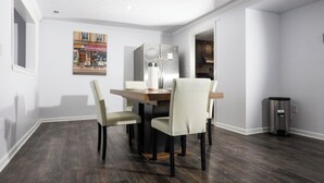 Un coin repas avec une table et des chaises en bois, une poubelle et un tableau accroché au mur.