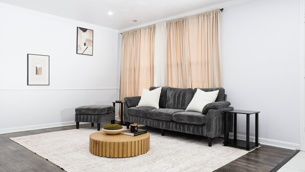 Un salon moderne avec un canapé d’angle gris, une table basse ronde en bois et un tapis blanc.
