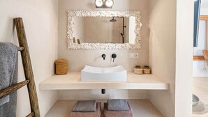 A bathroom with a white sink, a mirror with a stone frame, a shower, and a towel rack. - Hilltop Oceanview Escape | Private Pool (Kralendijk)