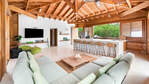 A spacious living area with a high ceiling, a large sofa, a coffee table, and a kitchen area with bar stools. - Hilltop Oceanview Escape | Private Pool (Kralendijk)