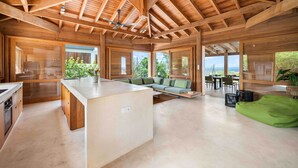 A spacious interior with a high ceiling, wooden beams, a central island, a green bean bag, and large windows offering views. - Hilltop Oceanview Escape | Private Pool (Kralendijk)