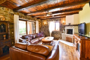 Ein gemütliches Wohnzimmer mit Kamin aus Stein, Ledersofas und einem Fernseher.