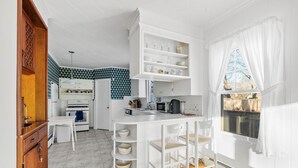 Une cuisine compacte avec des meubles blancs, un îlot central doté de tabourets, un four à micro-ondes et un évier.