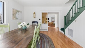 Un coin repas avec une table en bois, des chaises et un vase de fleurs. Il y a une carte accrochée au mur et un escalier avec des rampes vertes.