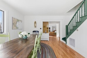 Ein Essbereich mit einem Holztisch, Stühlen und einer Blumenvase. An der Wand hängt eine Karte und eine Treppe mit grünen Geländern.