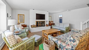 Un salon spacieux avec une cheminée, des meubles en osier vert et un canapé à motifs floraux.