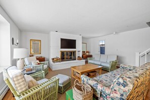 Ein geräumiges Wohnzimmer mit Kamin, grünen Korbmöbeln und einem Blumensofa.
