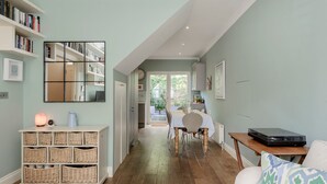 A cozy living room with a dining area, a bookshelf, and a table with a laptop. - Wild Roses in London (London)