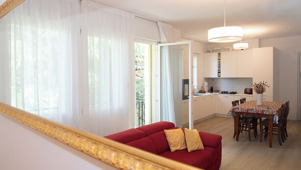Un salon moderne avec un canapé rouge, une table à manger avec des chaises et un coin cuisine visible à travers une porte ouverte.