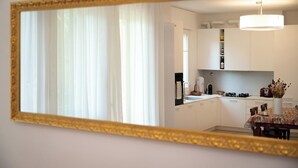 Une cuisine moderne avec des meubles blancs, une table à manger recouverte d’une nappe colorée et un grand miroir avec un cadre doré.